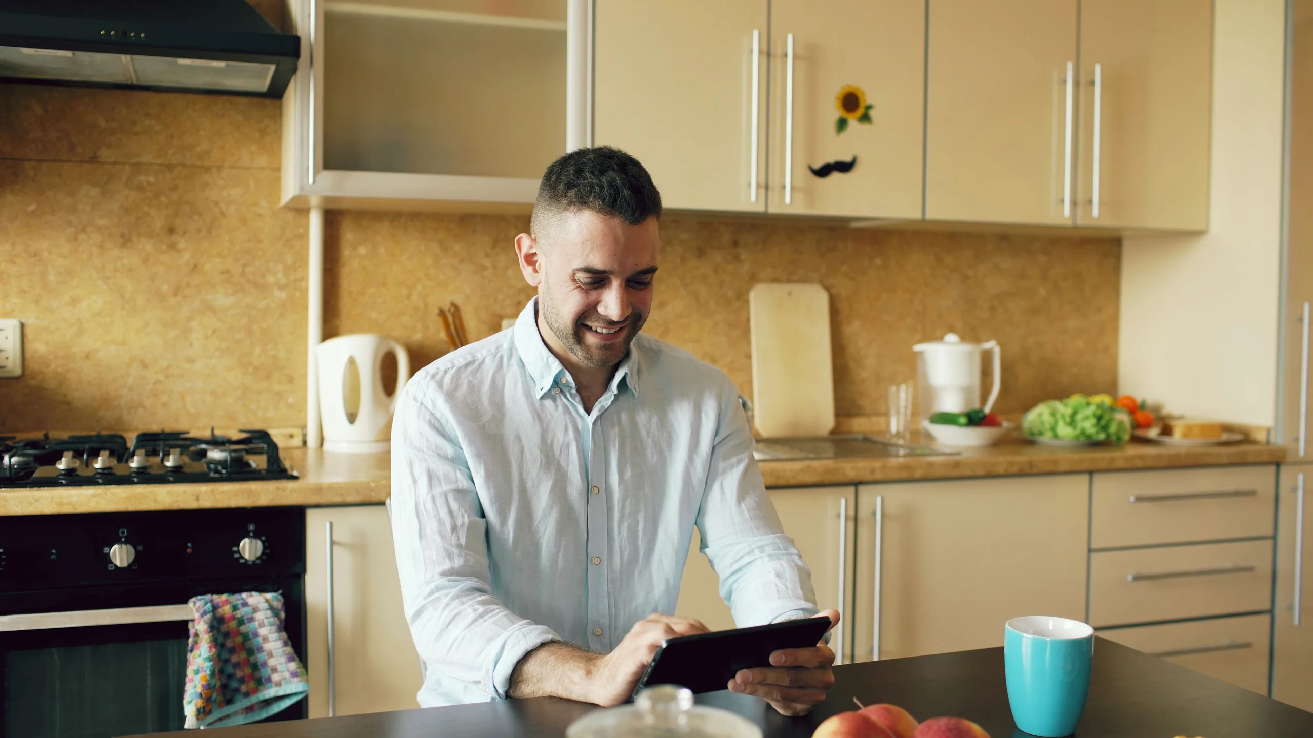 A man reading on a tablet at his kitchen table in the morning