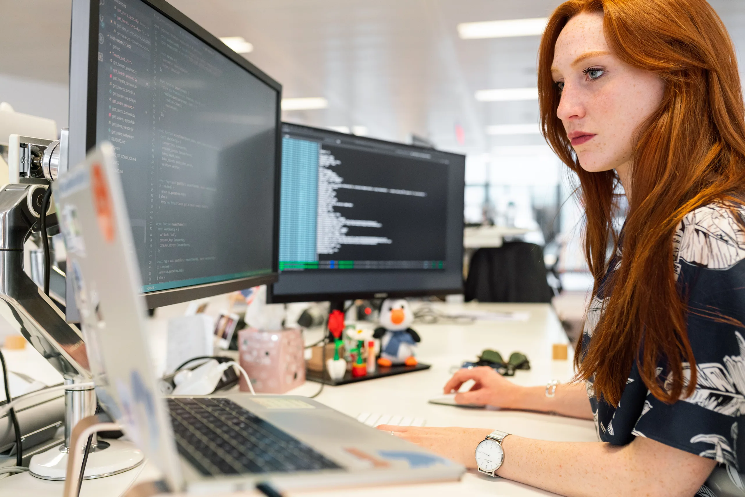 An engineer reviewing code on two monitors in a bright office