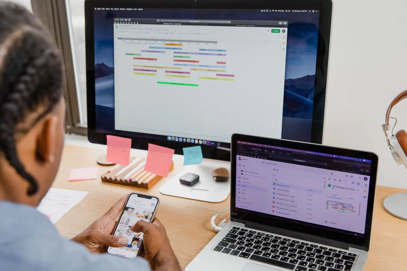 A person at a desk working across a laptop, a phone and a second screen at the same time