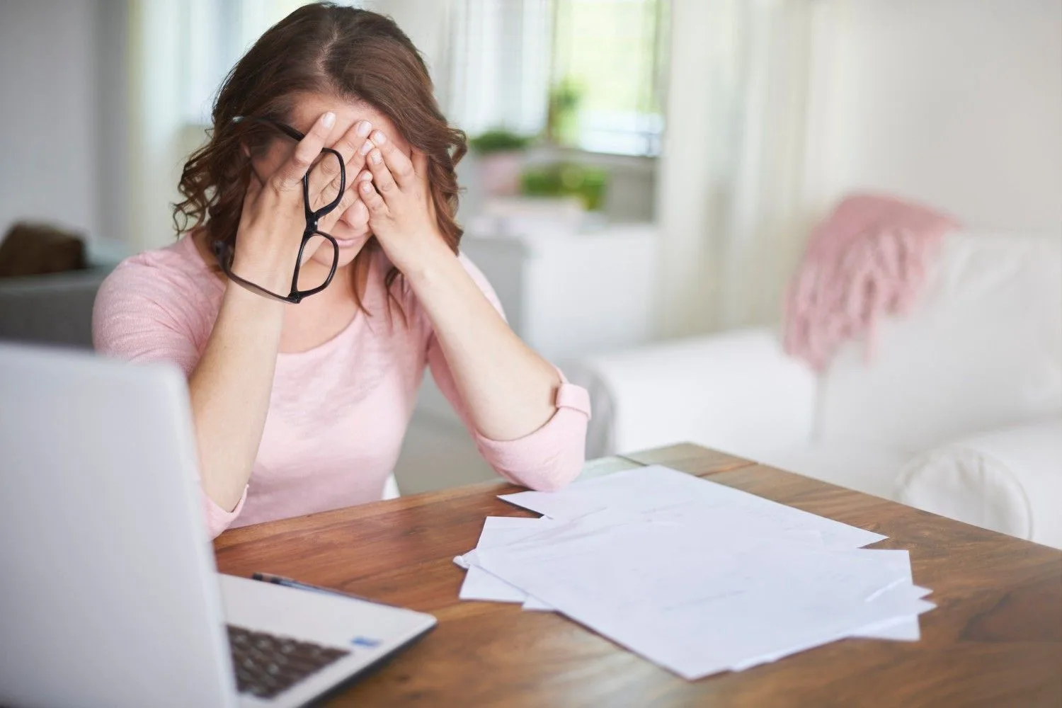 An accountant at a desk surrounded by paperwork and a laptop, head in hand